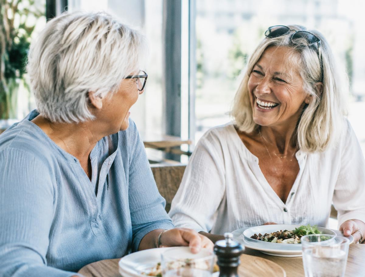 Two senior friends laughing over lunch at a cafe